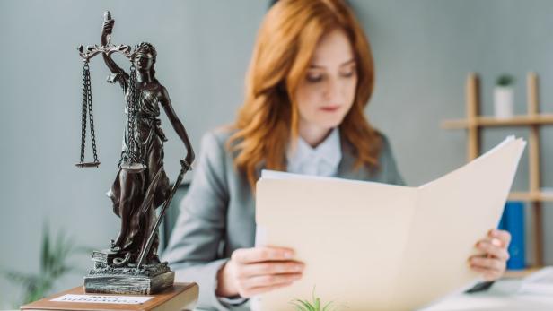 Female lawyer looking at folder, while sitting at workplace with themis figurine on pile of books on blurred background