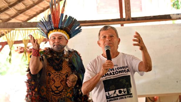 Zwei Männer, einer traditionell gekleidet, sprechen bei einer Versammlung im Amazonasgebiet.