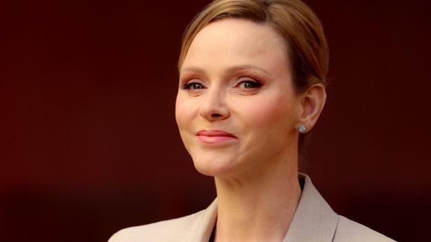 Fürstin Charlene mit blonden Haaren und hellem Blazer lächelt leicht.