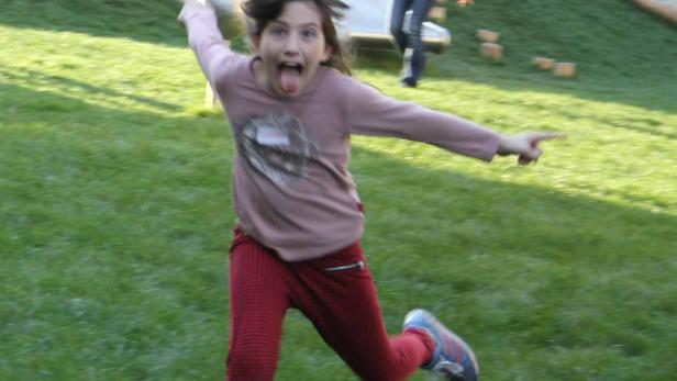 Ein Mädchen rennt auf einer Wiese und streckt die Zunge heraus.