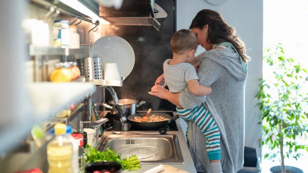 Mother carrying toddler on hip and preparing meal