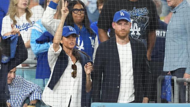 Meghan und Harry, beide mit "LA"-Kappen, schauen ein Baseballspiel an, Meghan jubelt.