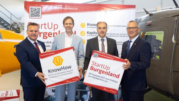 Vier Männer in Anzügen stehen vor einem Werbebanner von StartUp Burgenland und halten große Infotafeln in den Händen.