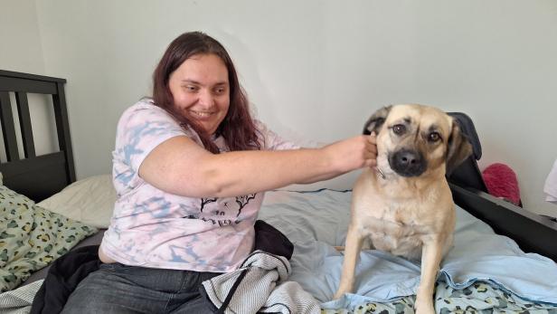 Frau sitzt mit einem Hund auf dem Bett