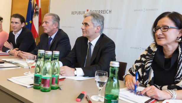 Mehrere Personen sitzen an einem Tisch vor dem Hintergrund der Flagge Österreichs.