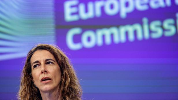Eine Frau mit welligem Haar spricht vor dem Hintergrund der Europäischen Kommission.