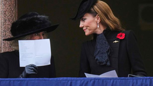 Camilla und Kate, beide mit Hüten und dunkler Kleidung, stehen auf einem Balkon.