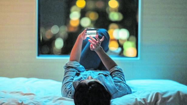 Woman lying down on bed and using smart phone at night