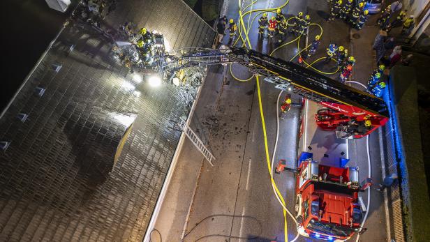 Eine Drohnenaufnahme von den Feuerwehrmitgliedern im Einsatz. Zu sehen ist der geöffnete Dachstuhl und die Straße, auf der sich Menschen in Feuerwehrkleidung tummeln.