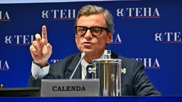 Ein Mann im Anzug spricht am Rednerpult, hebt einen Finger und sitzt vor einem Namensschild mit der Aufschrift „CALENDA“.