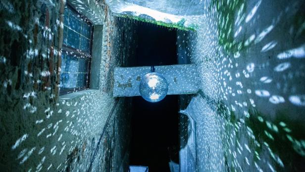 Eine Aufnahme von einer Discokugel von unten, die Licht auf die sie umgebenden Häuserwände projeziert.