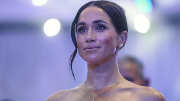 Herzogin Meghan, mit hochgestecktem Haar und Halskette, blickt aufmerksam zur Seite.