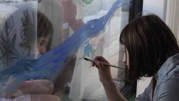 Eine Frau und ein Kind bemalen ein Fenster mit blauer Farbe.