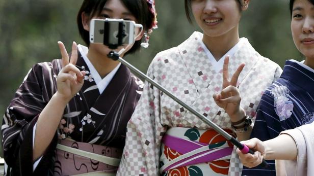 Drei junge Frauen in Kimonos machen ein Selfie mit einem Selfie-Stick und zeigen das Victory-Zeichen.