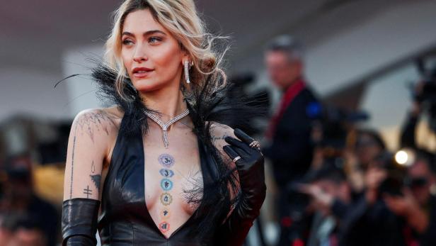 Paris Jackson trägt ein schwarzes Kleid mit Federn und Schmuck, ihre Tattoos sind sichtbar.