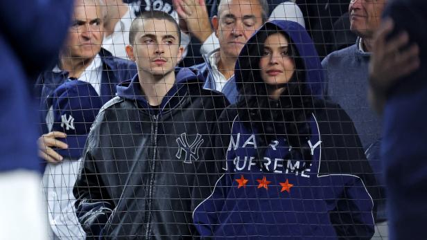 Kylie Jenner und Timothee Chalamet mit Kapuzen sitzen hinter einem Gitter bei einem Yankees-Spiel.