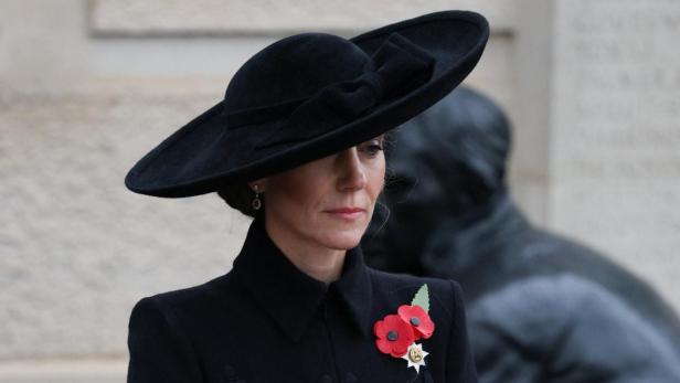 Prinzessin Kate, mit einem Schleierhut und einer Perlenkette, blickt gesenkt.