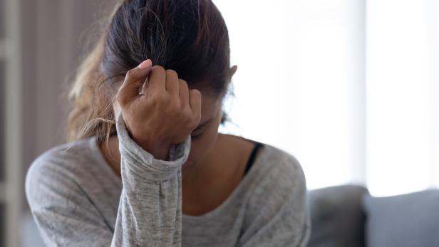 Eine Frau sitzt mit gesenktem Kopf und hält sich die Stirn, wirkt nachdenklich oder besorgt.