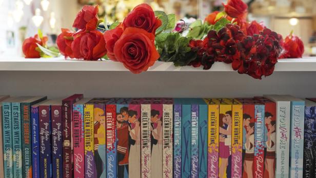 Rote Rosen und andere Blumen liegen auf einem Regal, darunter stehen bunte Liebesromane in einer Reihe.