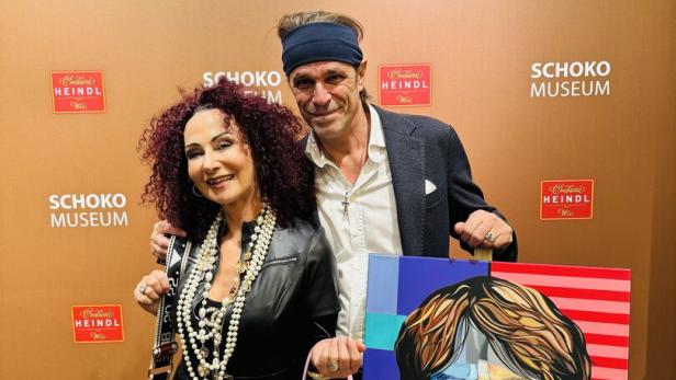 Zwei Personen posieren vor einer braunen Wand mit Pop-Art-Gemälden von Mick Jagger und Marilyn Monroe.