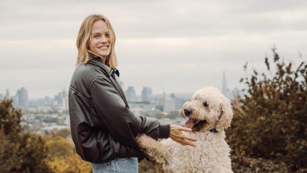 Ein beiger, wuscheliger Hund, wie er mit Moderatorin Mirjam Weichselbraun auf einer Wiese spielt