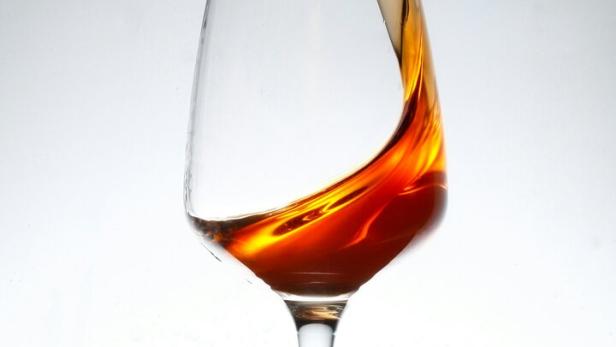 Ein Weinglas steht auf einer nassen Oberfläche und eine braune Flüssigkeit schwappt heraus