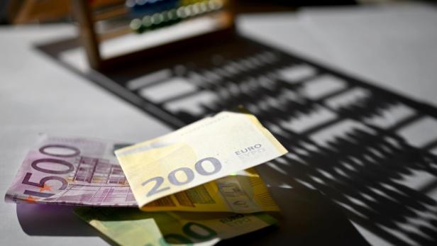 Euroscheine (500, 200, 100) liegen auf einem Tisch, im Hintergrund ein Rechenrahmen.