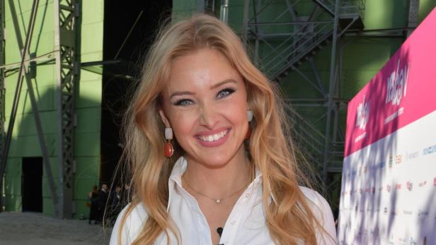 Patrice Aminati lächelt auf einem pinken Teppich bei einer öffentlichen Veranstaltung.