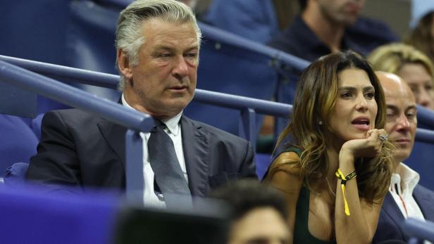 Alec Baldwin im Anzug und Hilaria Baldwin mit langen Haaren sitzen nebeneinander auf Tribünen und schauen aufmerksam nach vorn.