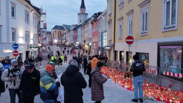 Viele Menschen versammeln sich an einer abgesperrten Straße, umgeben von zahlreichen Kerzen und Blumen zum Gedenken.