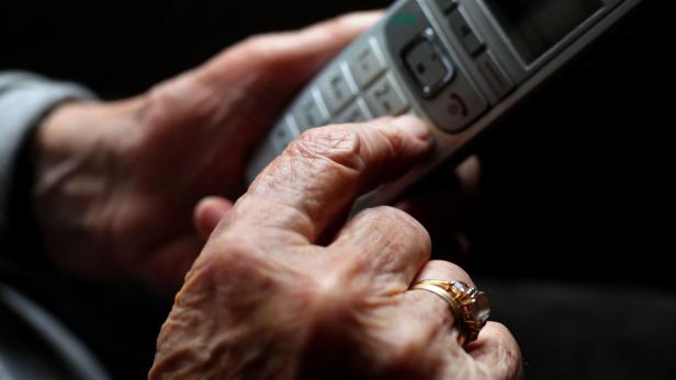 Eine ältere Hand mit Ring tippt auf die Tasten eines schnurlosen Telefons.