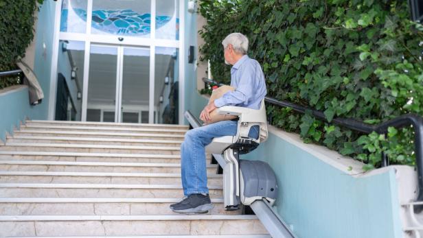 Mann fährt mit dem Treppenlift zum Haustor