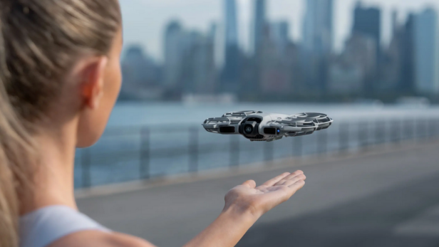Eine Frau steuert die DJI Neo 2 Drohne per Handgeste am Ufer einer Großstadt.