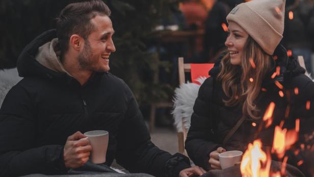 Ein Mann und eine Frau wärmen sich an einem Lagerfeuer. 