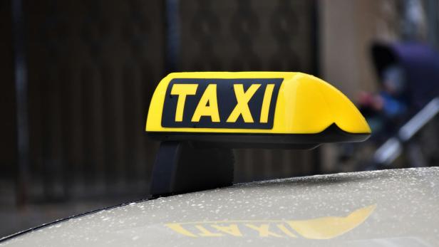 Gelbes TAXI-Dachzeichen auf einem Auto, im Hintergrund unscharf.