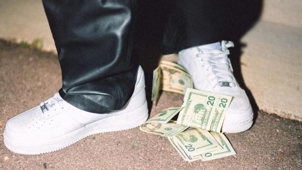 Weiße Sneaker steigen auf Geldscheine drauf.