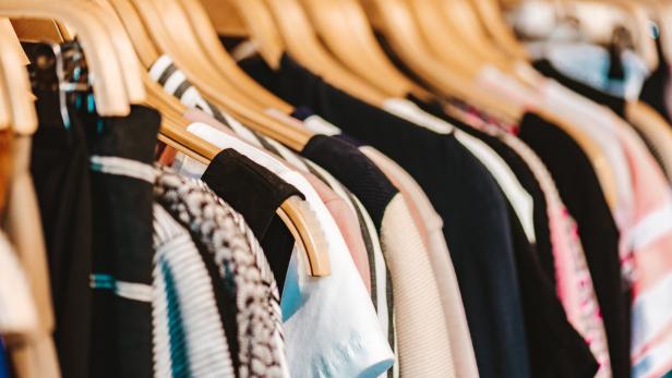 Mehrere bunte Kleidungsstücke hängen ordentlich auf Holzkleiderbügeln an einer Stange.