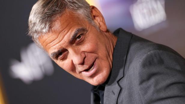 George Clooney lächelt in einem grauen Anzug vor einem unscharfen Hintergrund.
