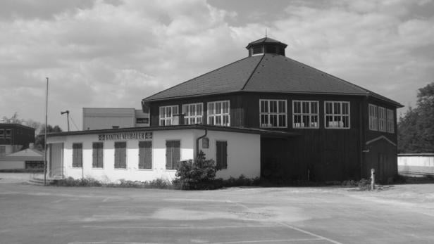 Ein achteckiges Gebäude mit vielen Fenstern und einem angebauten weißen Teil mit der Aufschrift „Kantine Neubauer“.