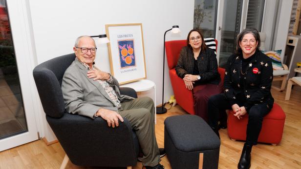 Drei Personen sitzen entspannt in einem modern eingerichteten Raum mit farbigen Sesseln und einem gerahmten Kunstwerk.