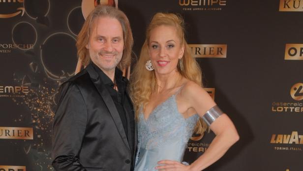 Ein Mann im schwarzen Anzug und eine Frau im hellblauen Abendkleid posieren gemeinsam auf einem roten Teppich.