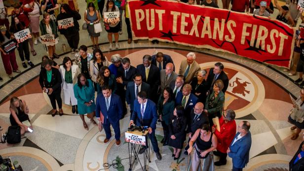 Eine Gruppe von Menschen steht mit einem Banner "PUT TEXANS FIRST" und Schildern in einem Gebäude.