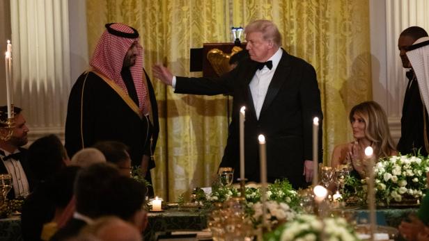 Donald Trump begrüßt einen Gast in traditioneller Kleidung bei einem formellen Dinner mit Melania Trump.