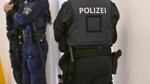 Eine Aufnahme von mehreren uniformierten Personen. Ein Mensch steht mit dem Rücken zur Kamera, auf der Weste ist "Polizei" zu lesen.