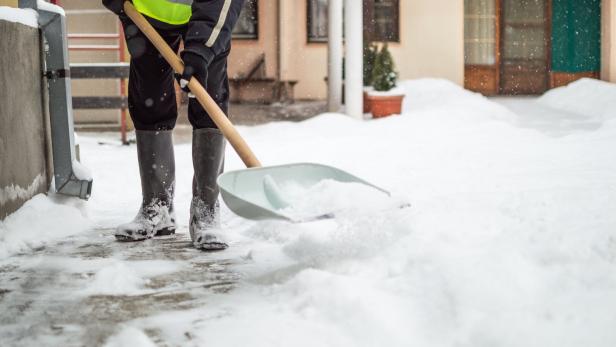 Mann schaufelt Schnee vom Gehsteig