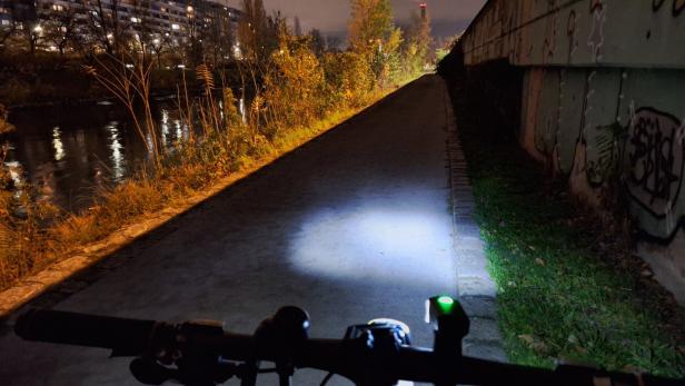 Lichtschein aus Rad-Beleuchtung fällt auf dunklen Asphalt des Donaukanals.  