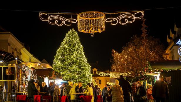 Menschen genießen einen festlich beleuchteten Weihnachtsmarkt mit geschmücktem Tannenbaum und Lichterketten bei Nacht.