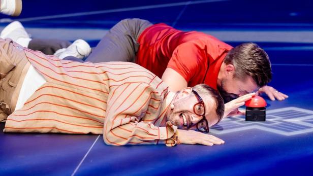 Joko & Klaas liegen auf dem Boden vor einem roten Buzzer