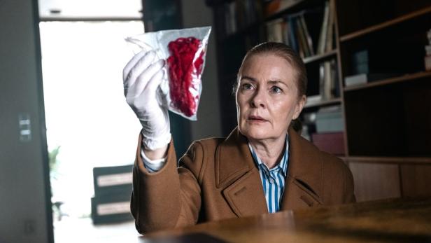 Frau betrachtet ein rotes Stoffteil in einem Beutel für Beweisstücke