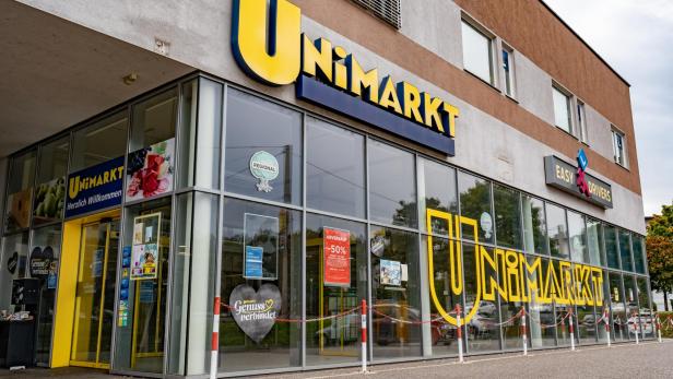 Die Fassade eines Unimarkt-Supermarkts mit großen Fensterfronten und gelber Beschriftung ist zu sehen.